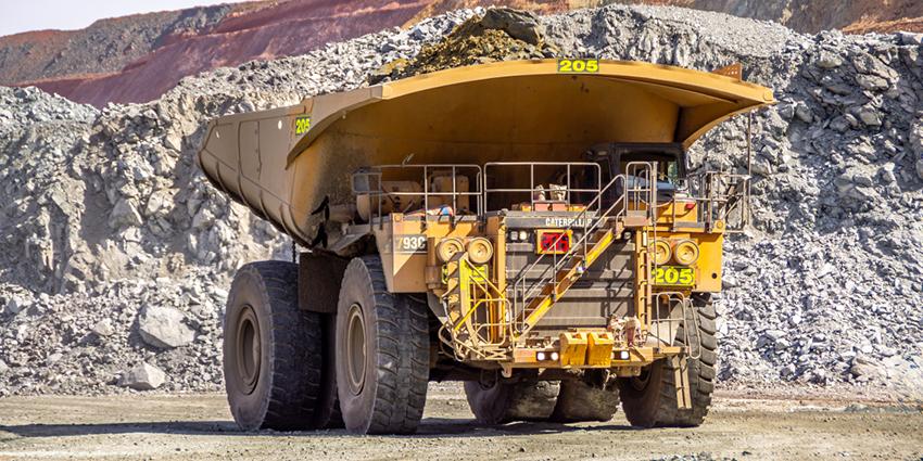 The image shows a large mining dump truck loaded with rocks in an open-pit mining environment.