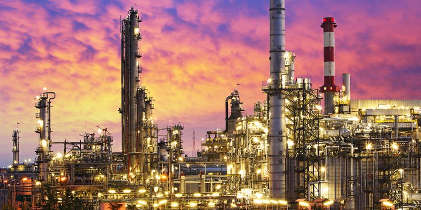 The image shows a large industrial refinery with tall structures and pipelines, illuminated against a colourful sunset