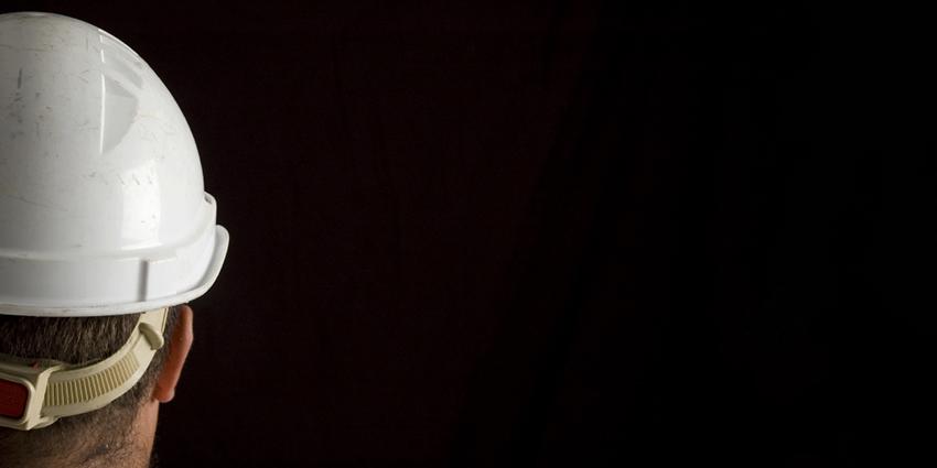 The image shows the back of a person's head wearing a white hard hat against a dark background